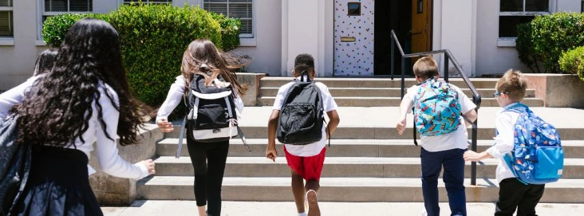 enfants avec sacs à dos vus de dos entrent à l'école